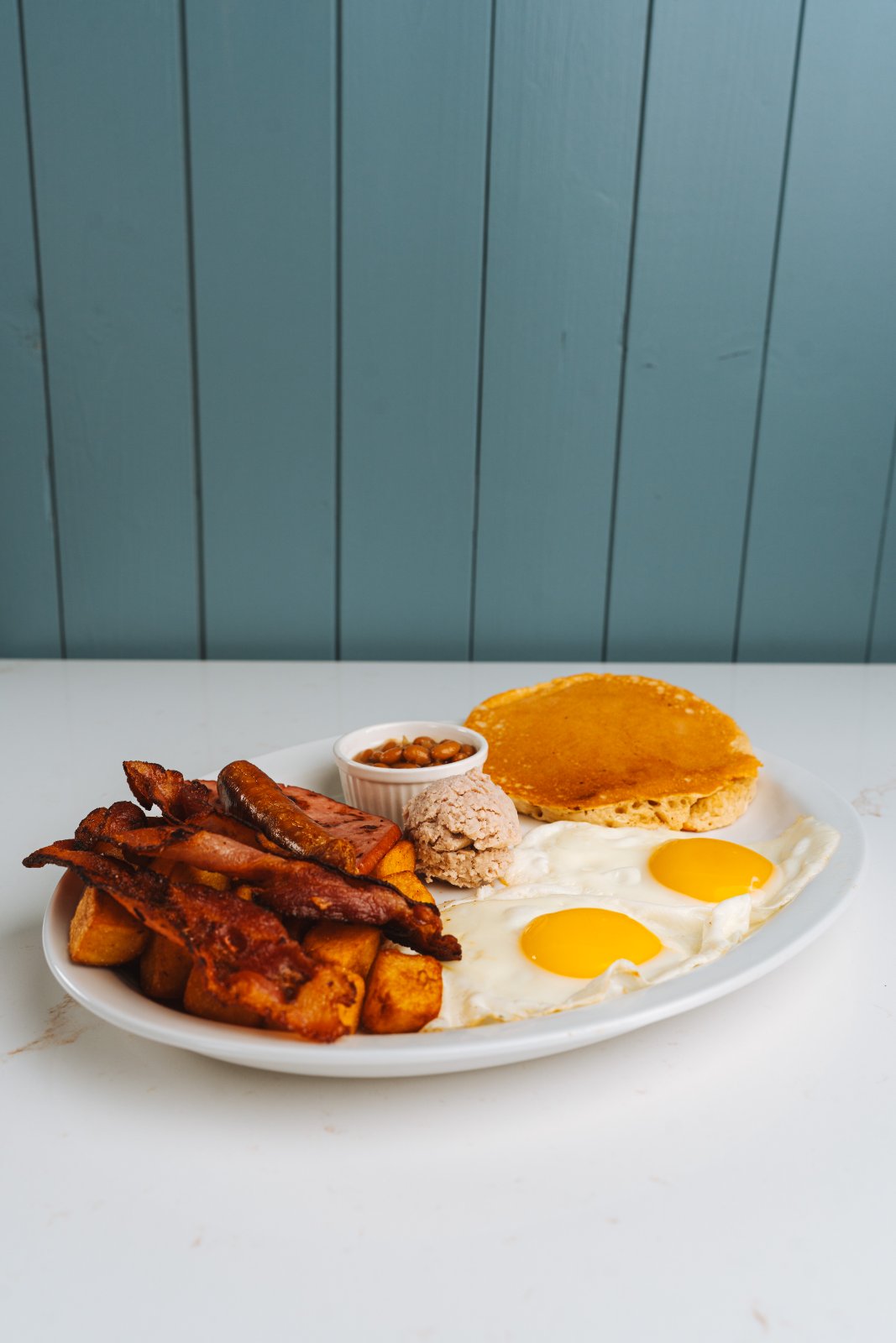 Assiette déjeuner : œufs, bacon, saucisse, pancake et fèves au lard — Suma, Delson